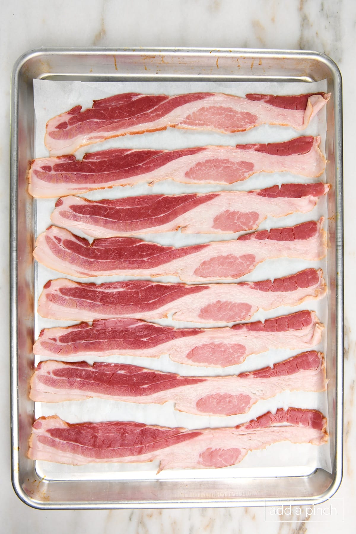 Photo of uncooked bacon on a parchment lined baking sheet.