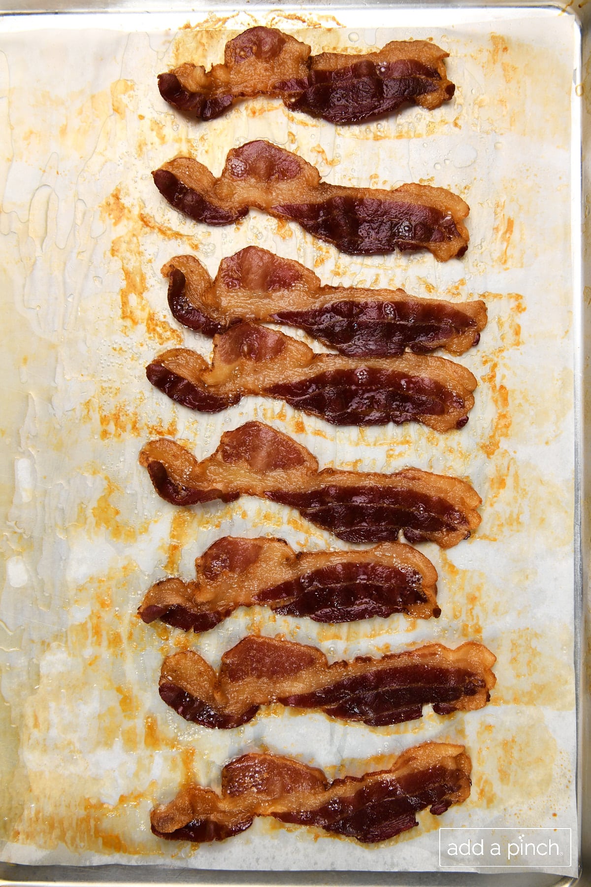 Photo of bacon cooked in the oven on a parchment lined baking sheet.