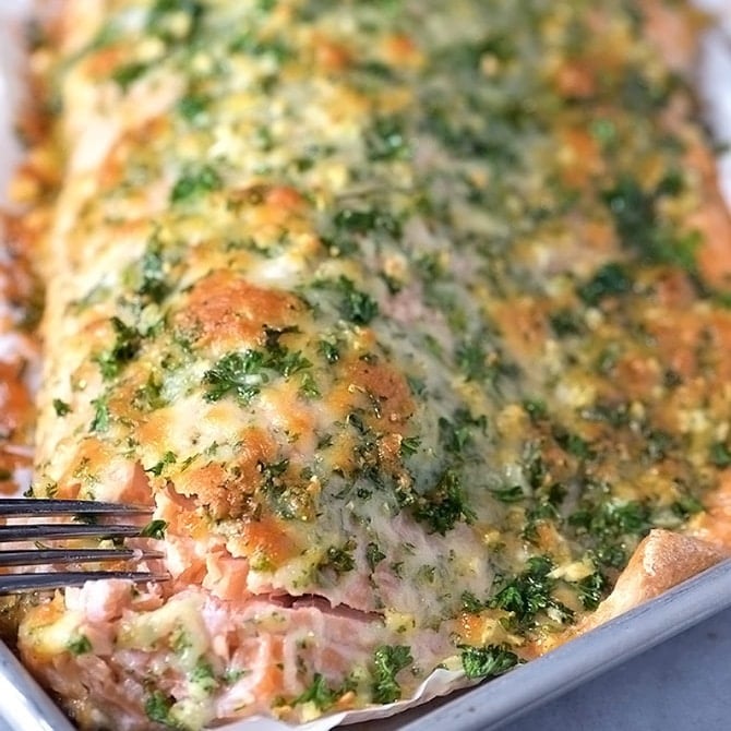 Baking sheet lined with parchment with Baked Salmon with Parmesan Herb Crust being flaked with a fork.