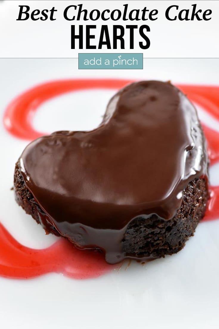 Heart shaped chocolate cake topped with ganache and raspberry sauce on a white serving dish - with text - addapinch.com