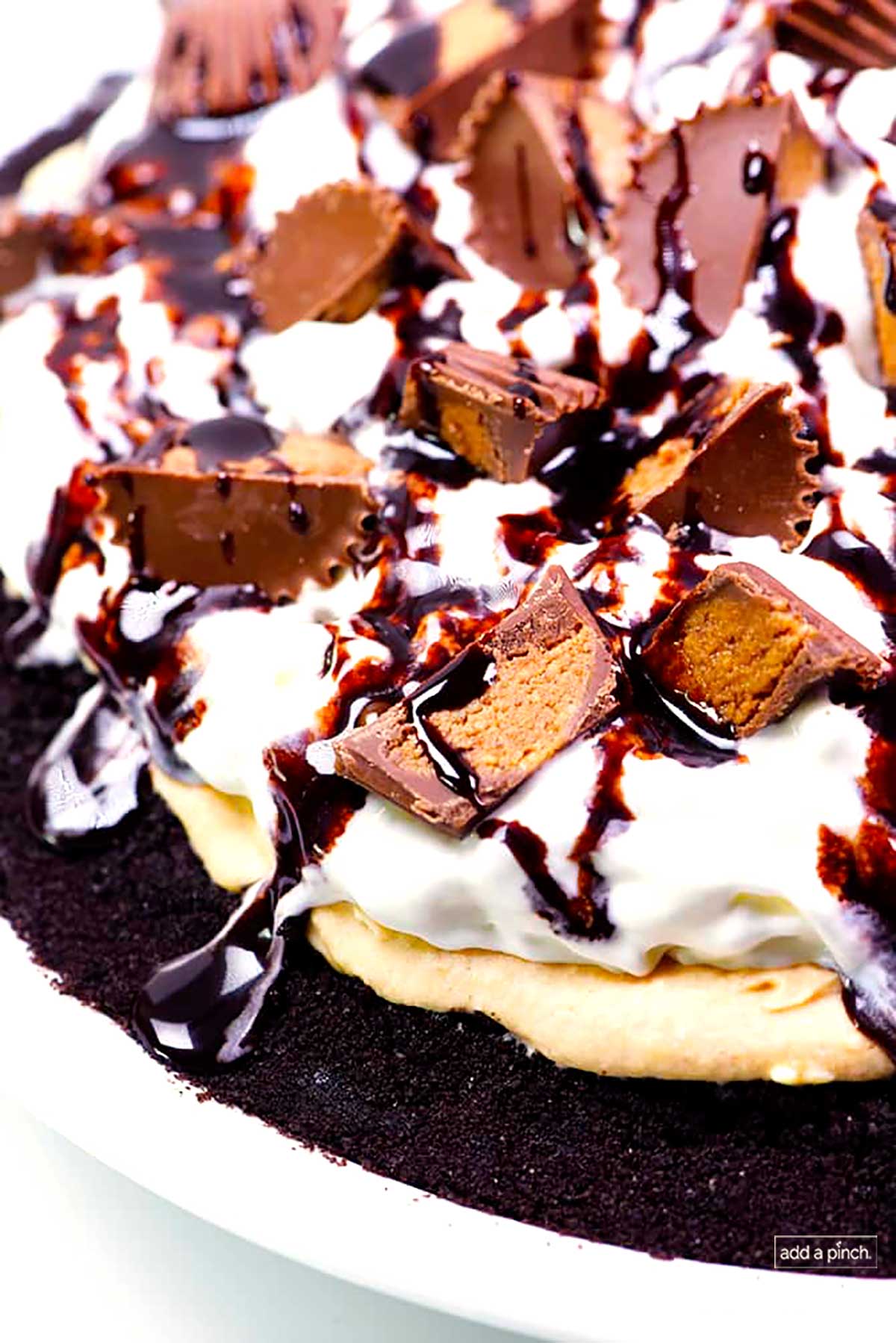 Photograph of peanut butter pie topped with peanut butter cups and chocolate syrup in a white pie plate.