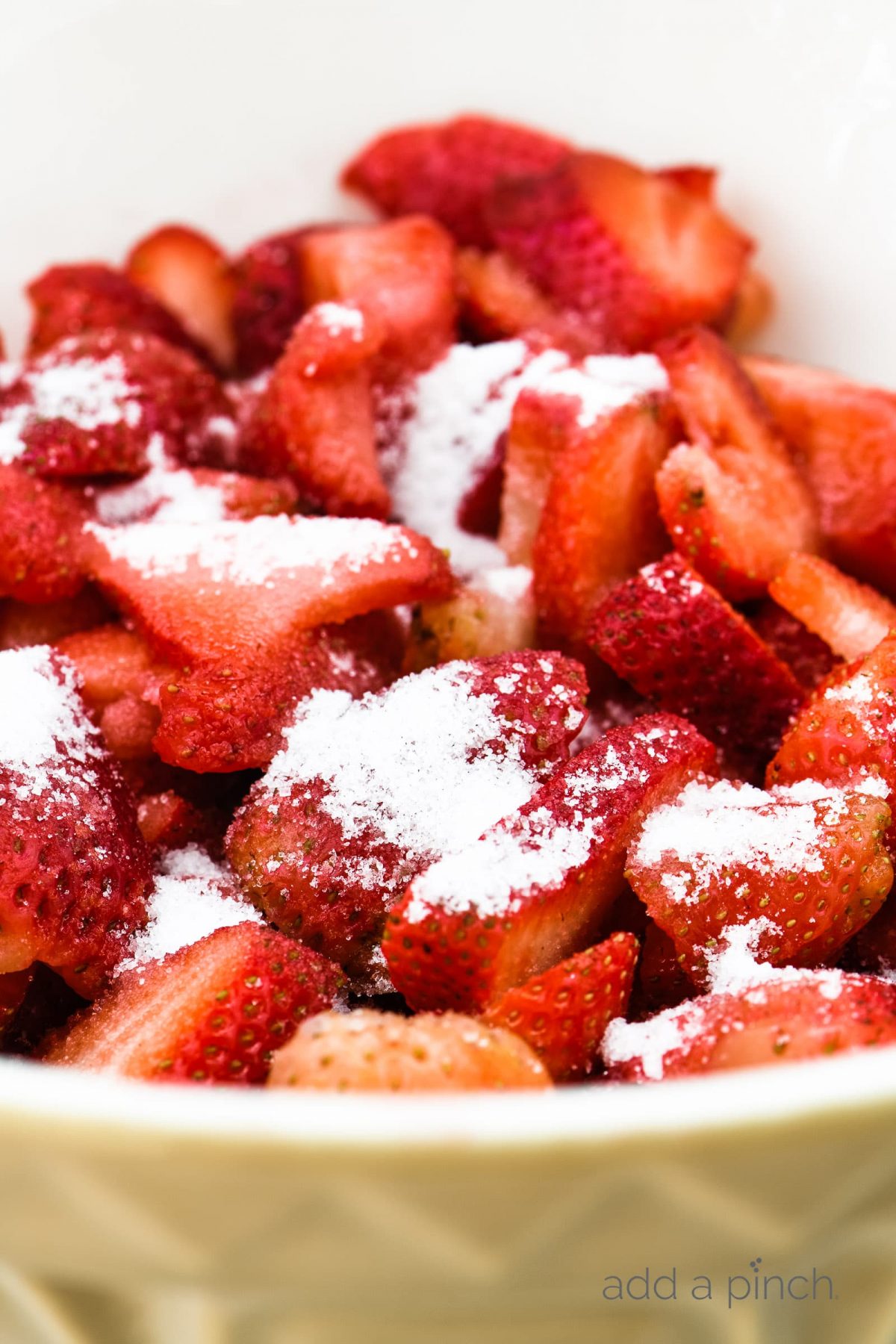Sliced strawberries with sugar in a large white bowl. // addapinch.com