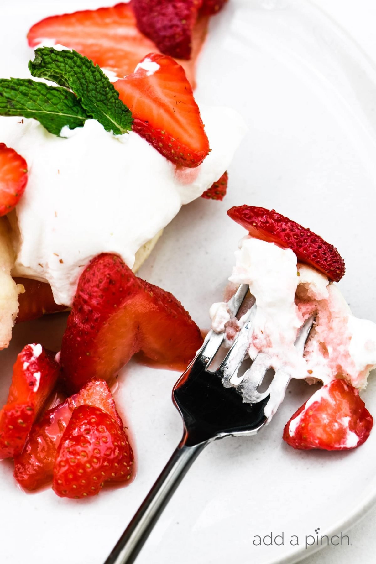 Strawberry shortcake, whipped cream, and strawberry slices on a white plate with a fork. // addapinch.com