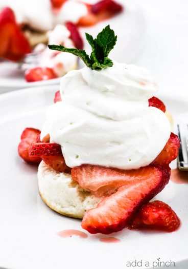 Strawberry shortcake topped with homemade whipped cream and mint sprig on a white plate. // addapinch.com