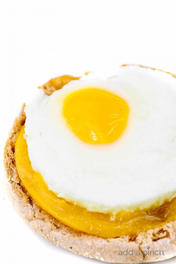 A bottom of an English muffin has some cheddar cheese and a baked egg on it // addapinch.com