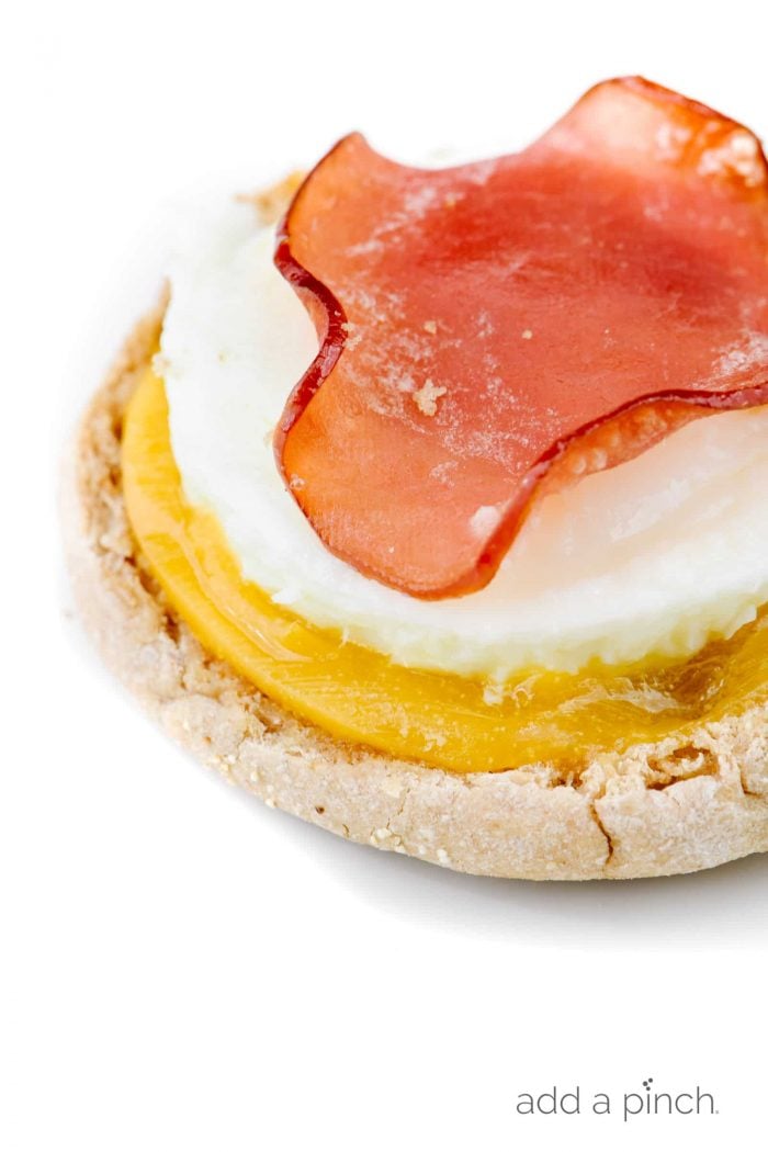 Botton of English muffin holds some melted cheese, baked egg and slice of Canadian bacon, with top of muffin missing // addapinch.com