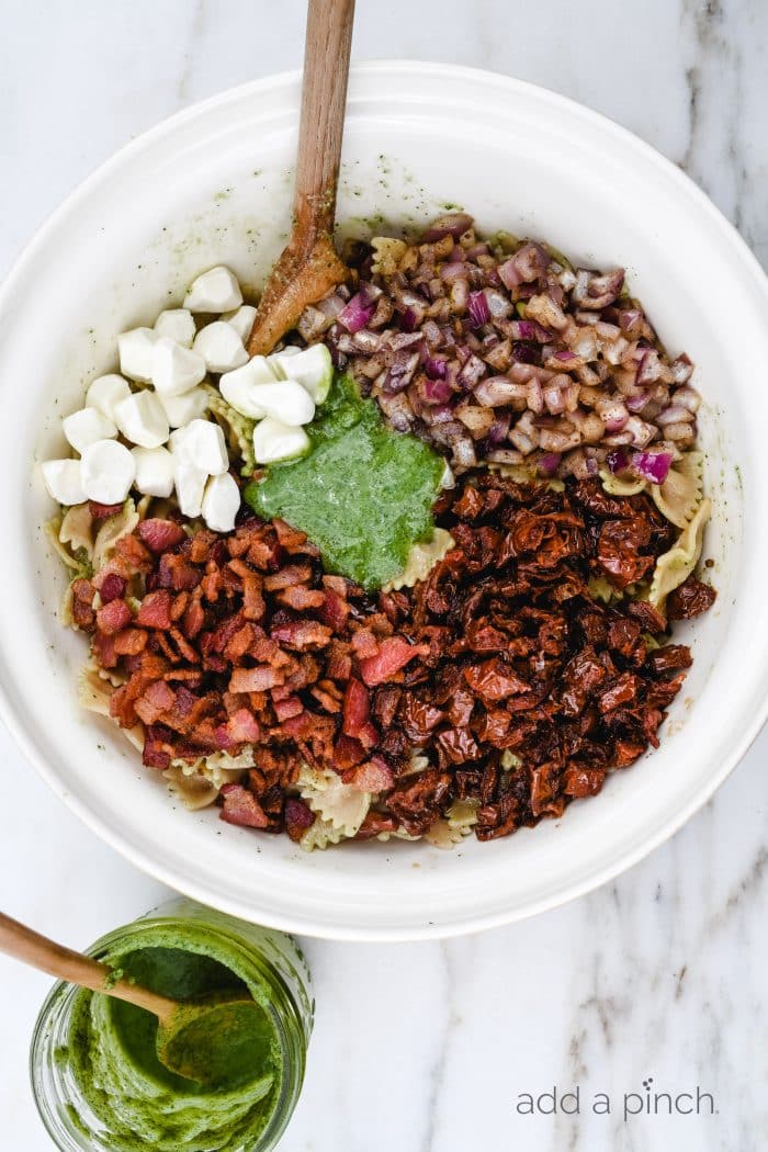 Pesto Caprese Pasta Salad Recipe - A classic pasta updated with a bright pesto dressing, sundried tomatoes, and bacon. A perfect quick and easy side dish! // addapinch.com