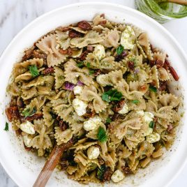 Pesto Caprese Pasta Salad Recipe - A classic pasta updated with a bright pesto dressing, sundried tomatoes, and bacon. A perfect quick and easy side dish! // addapinch.com