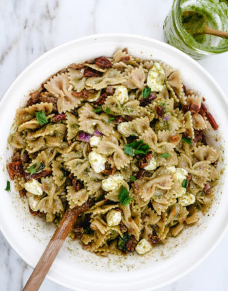 Pesto Caprese Pasta Salad Recipe - A classic pasta updated with a bright pesto dressing, sundried tomatoes, and bacon. A perfect quick and easy side dish! // addapinch.com