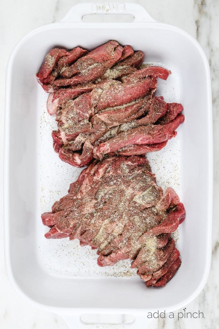 White baking dish with slices of sirloin steak sprinkled well with Stone House Seasoning // addapinch.com