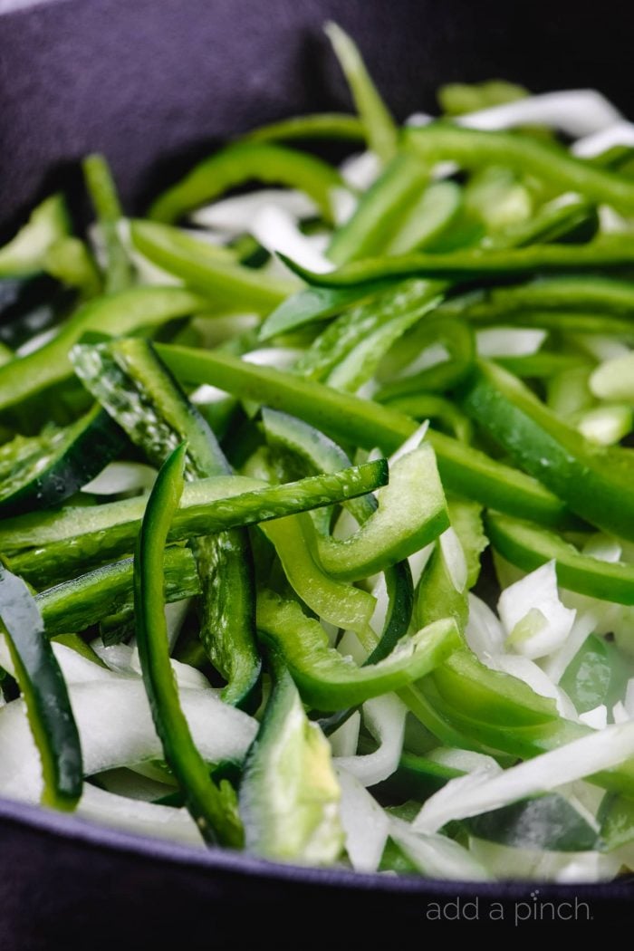 Thin slices of green peppers and onion in a black skillet // addapinch.com