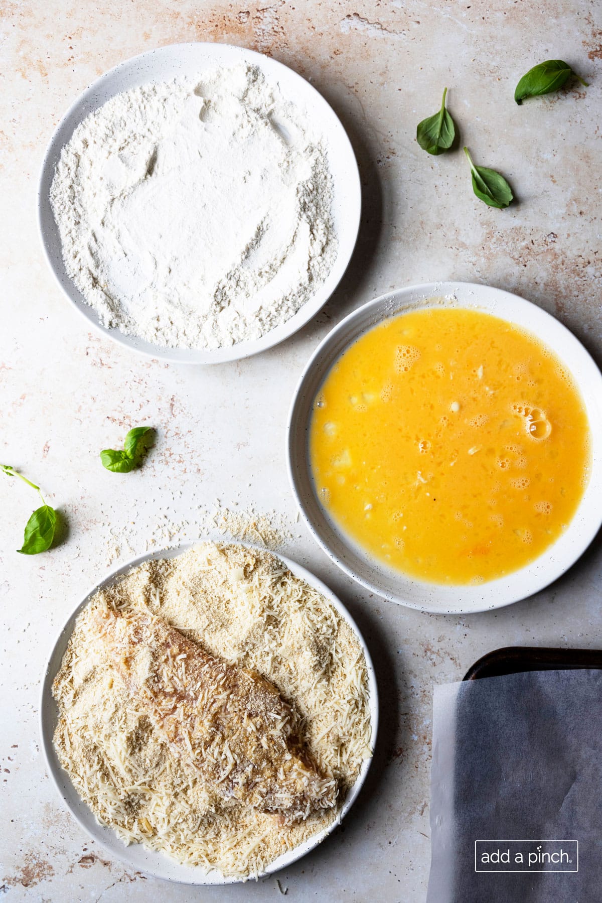 Image of three bowls used for coating chicken for chicken parmesan. Bowls are filled with flour, beaten eggs, and parmesan and panko.