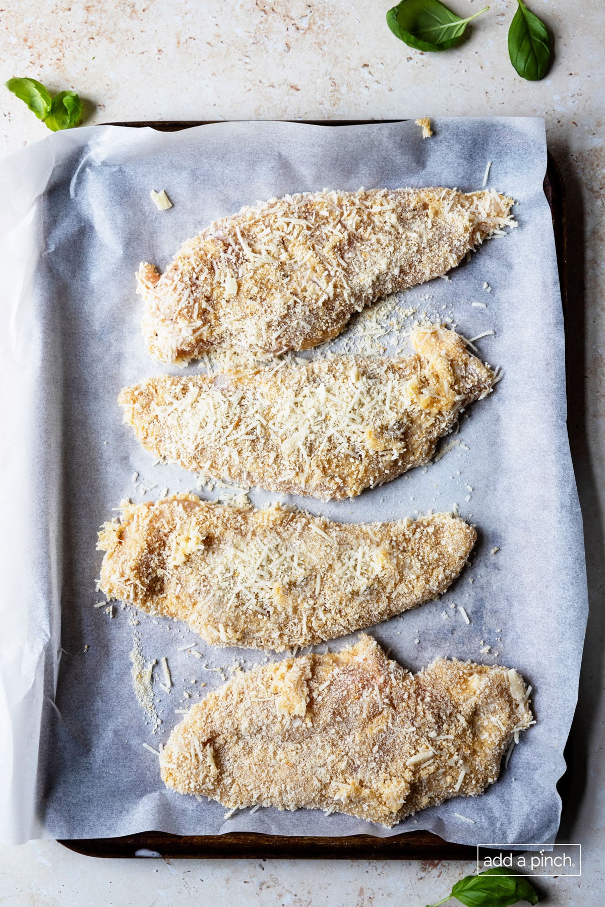Photo of coated chicken breasts on a piece of white parchment paper.