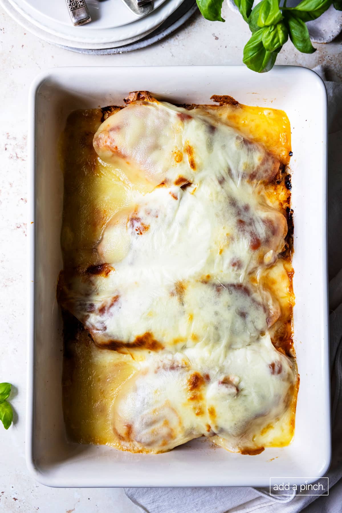 Photo of baked chicken parmesan in a white baking dish.