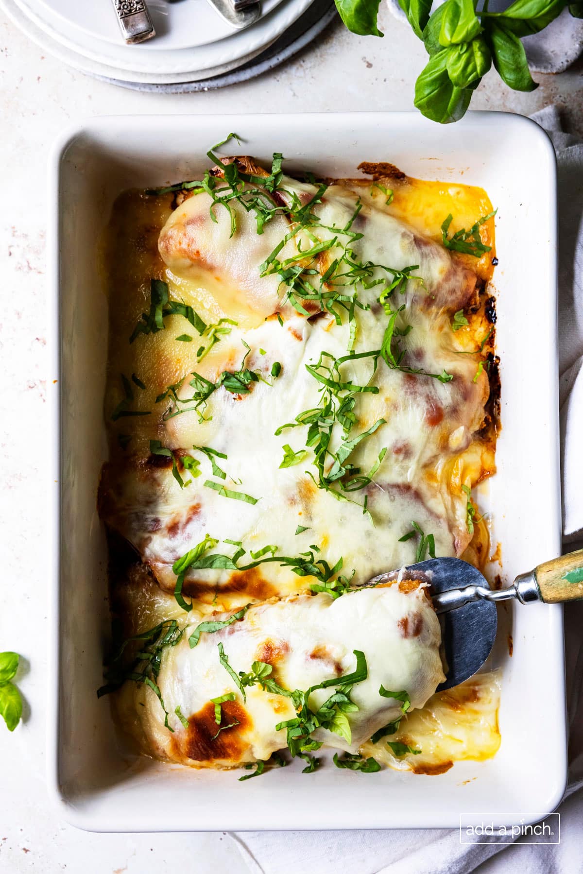 Photo of baked chicken parmesan topped with fresh basil in a white baking dish.