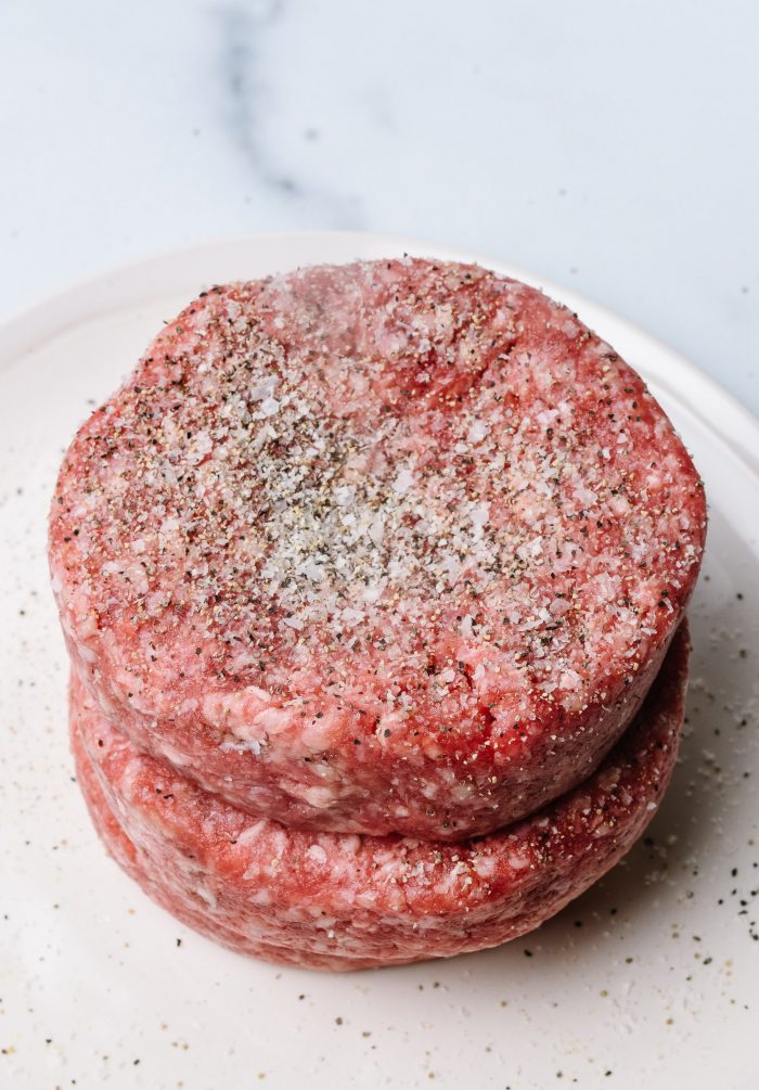 Ground chuck formed into three even thickness, 1/4 pound patties,   seasoned with Stone House Seasoning, on white plate // addapinch.com