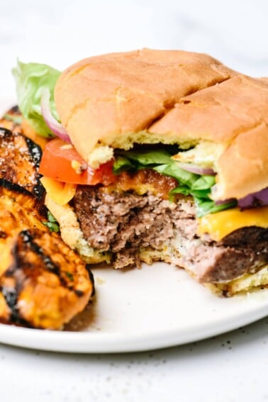 Hamburger with grilled sweet potatoes on a white plate.