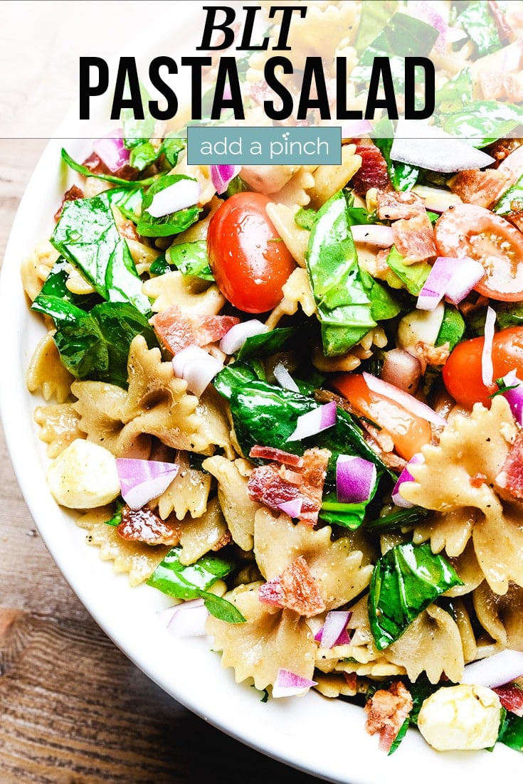 BLT Pasta Salad on a white dish sitting on a wooden table - with text - addapinch.com