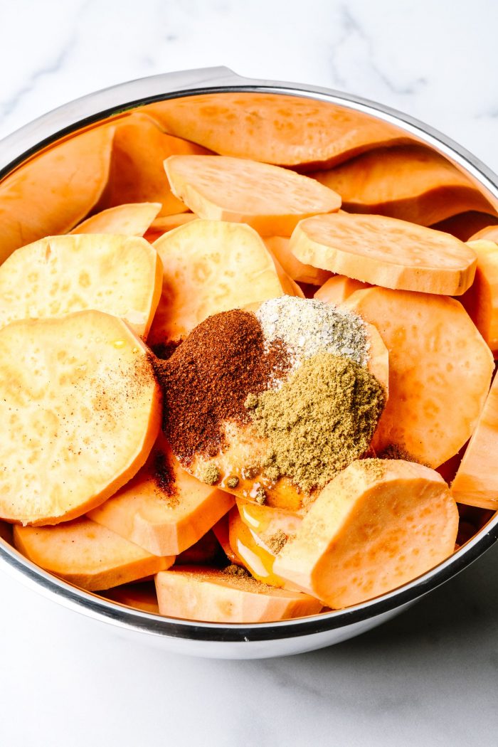 Slices of sweet potato with spices and olive oil in stainless bowl on marble countertop // addapinch.com