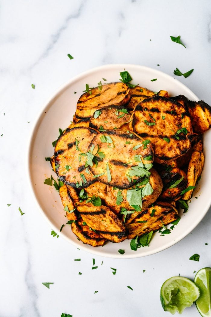 Slices of grilled sweet potatoes garnished with herbs, on a white plate // addapinch.com