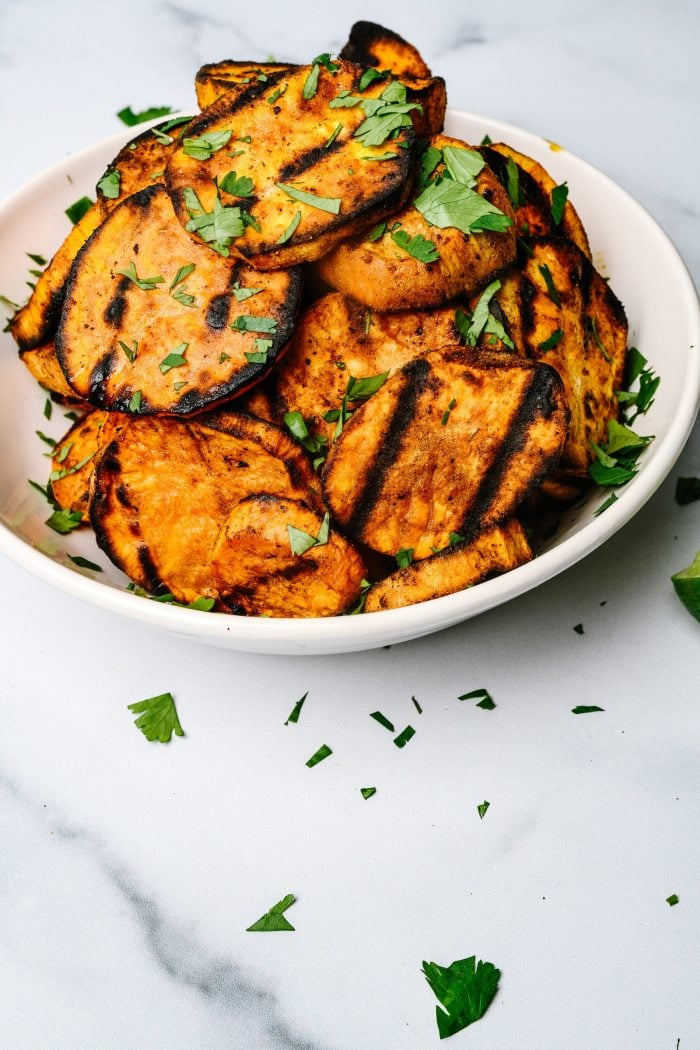 White bowl with grilled sweet potatoes surrounded by garnish and lime slices // addapinch.com 