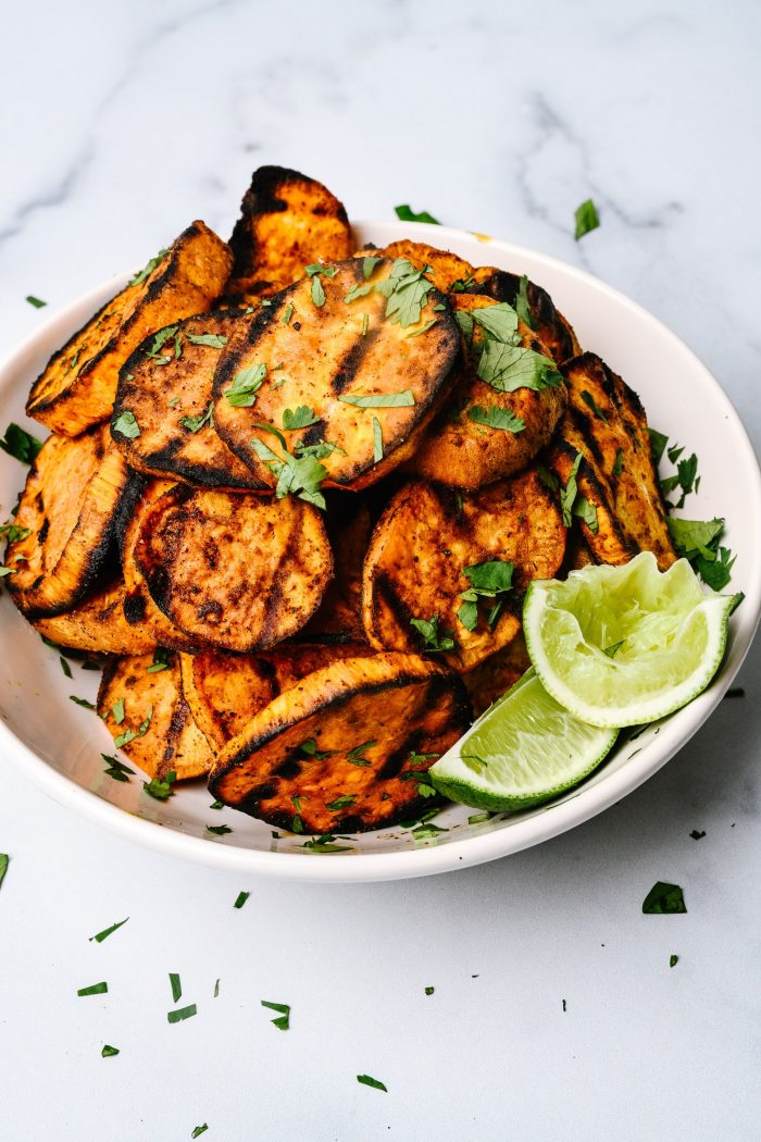 White plate with sweet potato slices that have been grilled, with lime slices on side of plate // addapinch.com