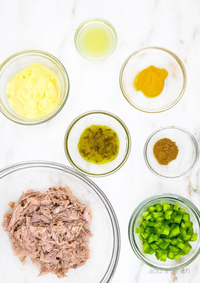 Tuna salad ingredients in clear glass bowls - tuna, mayo, mustard, pickle relish, curry and chopped celery. // addapinch.com