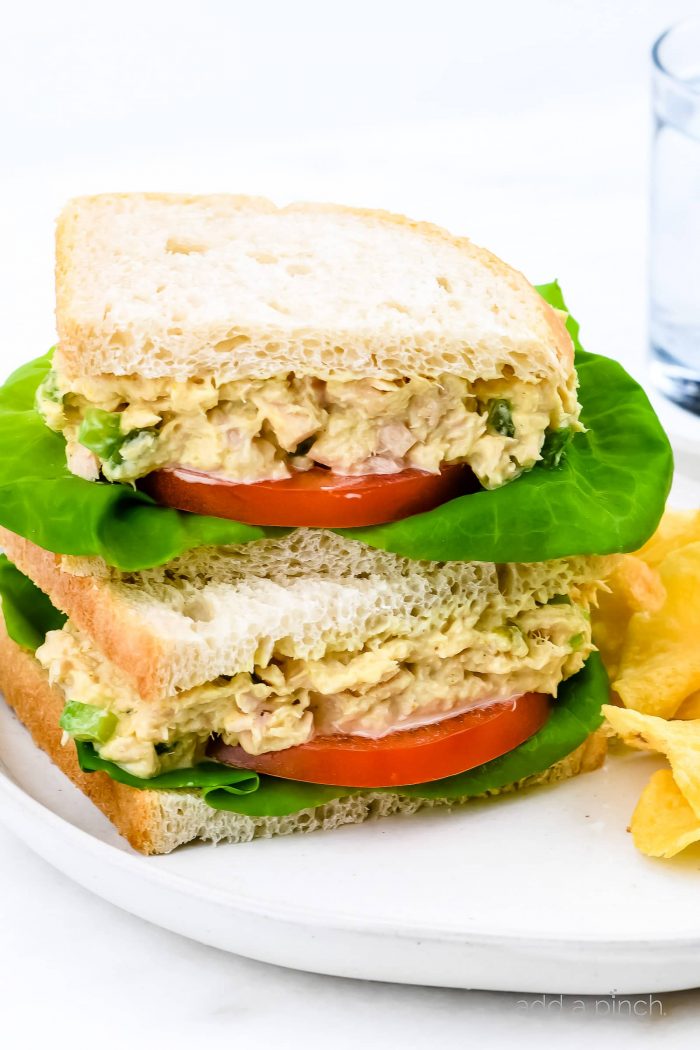 Tuna salad sandwich with lettuce and tomato slices with sandwich cut in half and stacked. Side of potato chips and glass of water  // addapinch.com