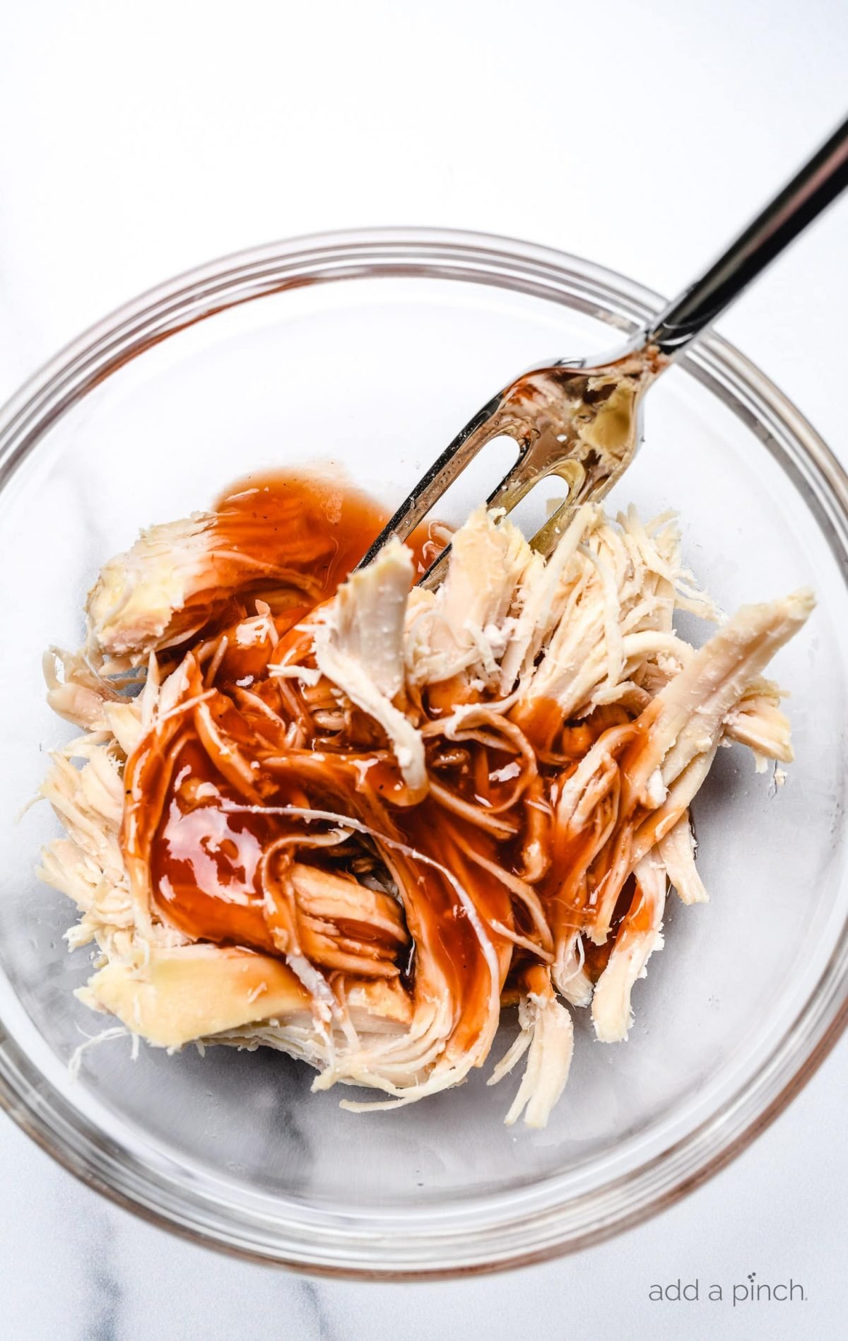 Shredded chicken in a glass bowl topped with BBQ Sauce.