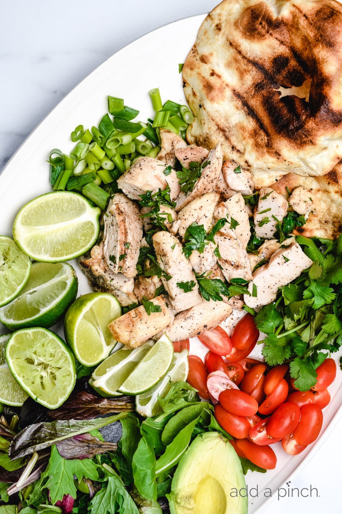 Salad topped with cilantro lime chicken on a platter with limes, cilantro, tomatoes and a tortilla. // addapinch.com