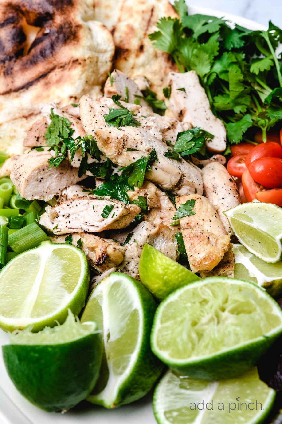 Lime halves on a platter with chicken, tomatoes and onions. 