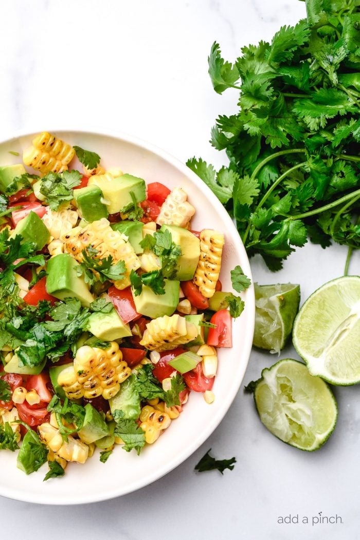 Fresh limes and cilantro surround a bowl of grilled corn salad // addapinch.com