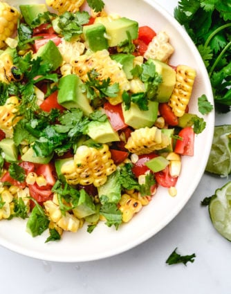 Grilled corn salad features fresh summer corn with avocado, tomato, jalapeno, and onion. A delicious, quick, easy and healthy recipe that is perfect for summer barbecues! // addapinch.com