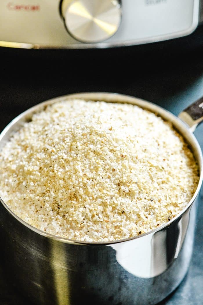 Stainless steel measuring cup full of stone-ground grits held in front of an instant pot // addapinch.com