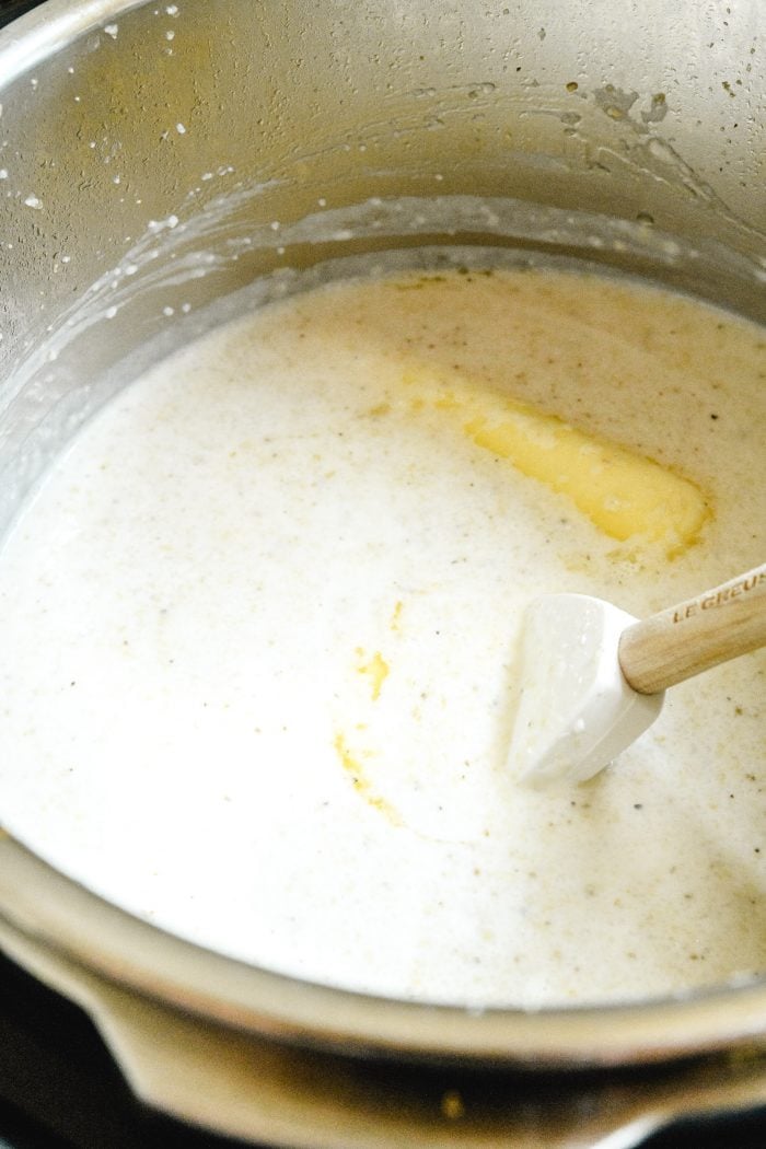 Cream and butter being mixed into grits in Instant Pot with wooden handled spoon // addapinch.com
