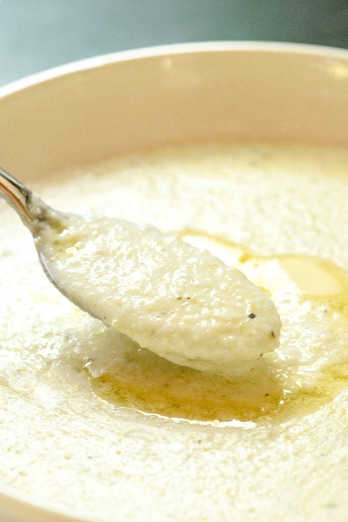 Close up photo of creamy, buttery grits on a spoon over a bowl of grits. // addapinch.com