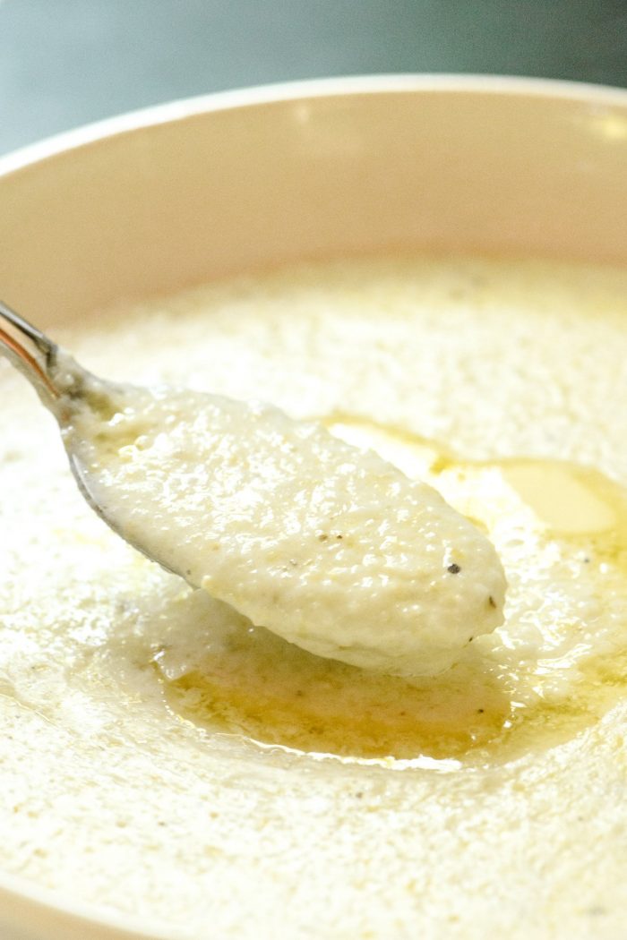 Close up photo of creamy, buttery grits on a spoon over a bowl of grits. // addapinch.com