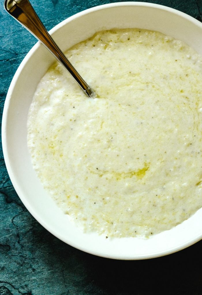 Creamy, buttery grits in a white bowl on a green background  //addapinch.com