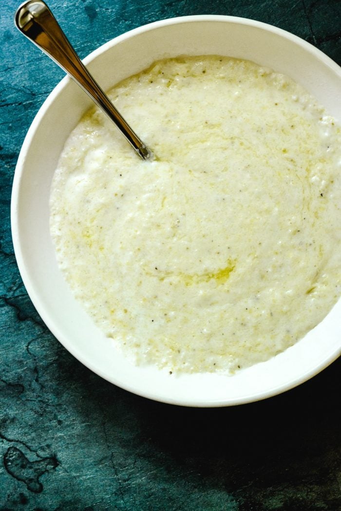 Grits with butter in a white bowl on a green background.