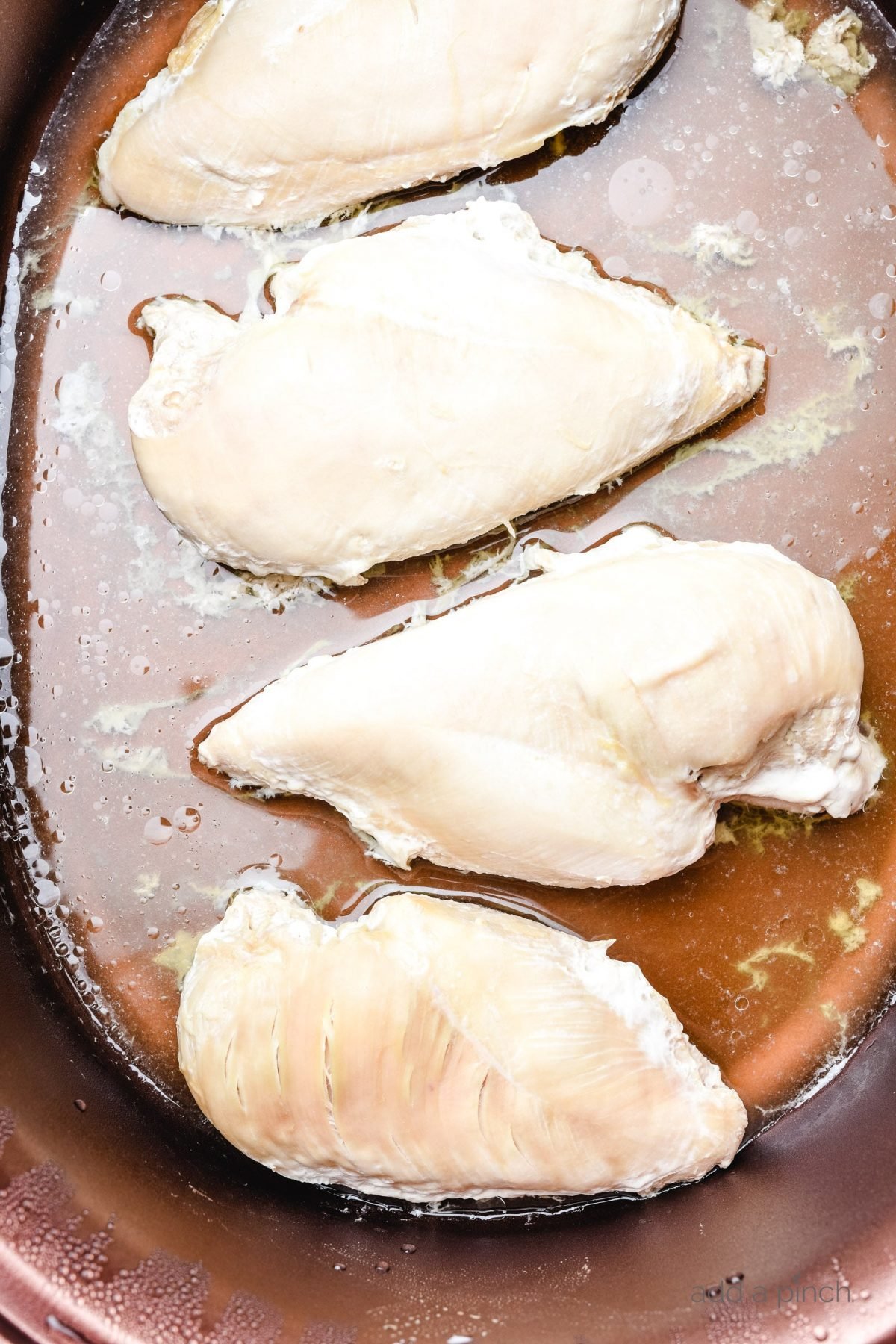 Four chicken breasts with liquid in a slow cooker.