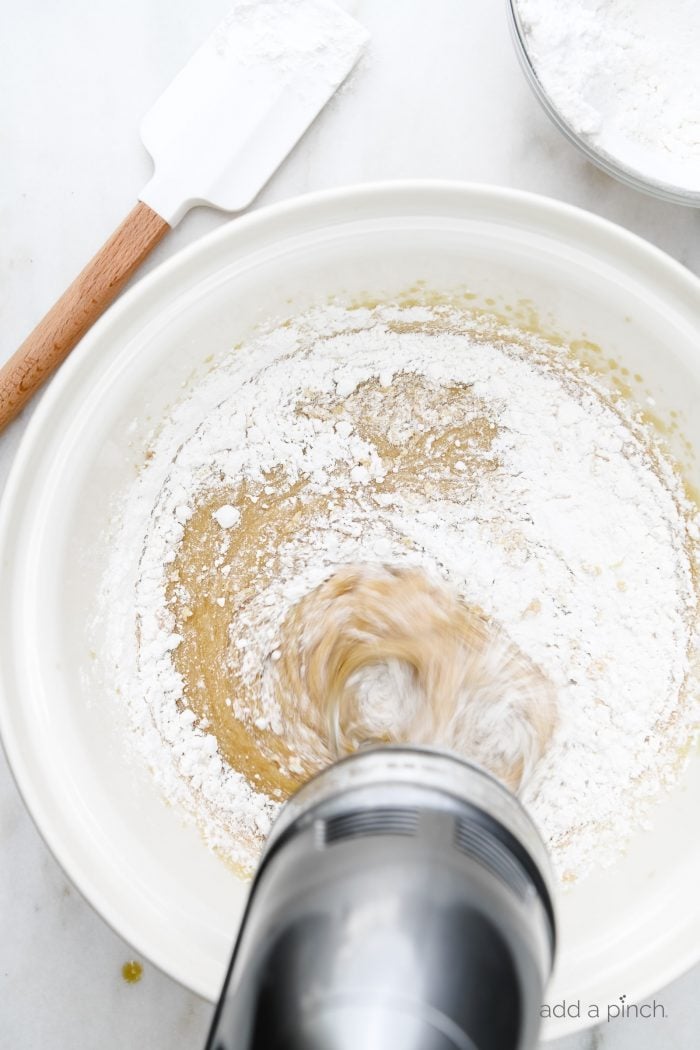 Using electric hand mixer to mix in self-rising flour into white mixing bowl with other blended ingredients. // addapinch.com