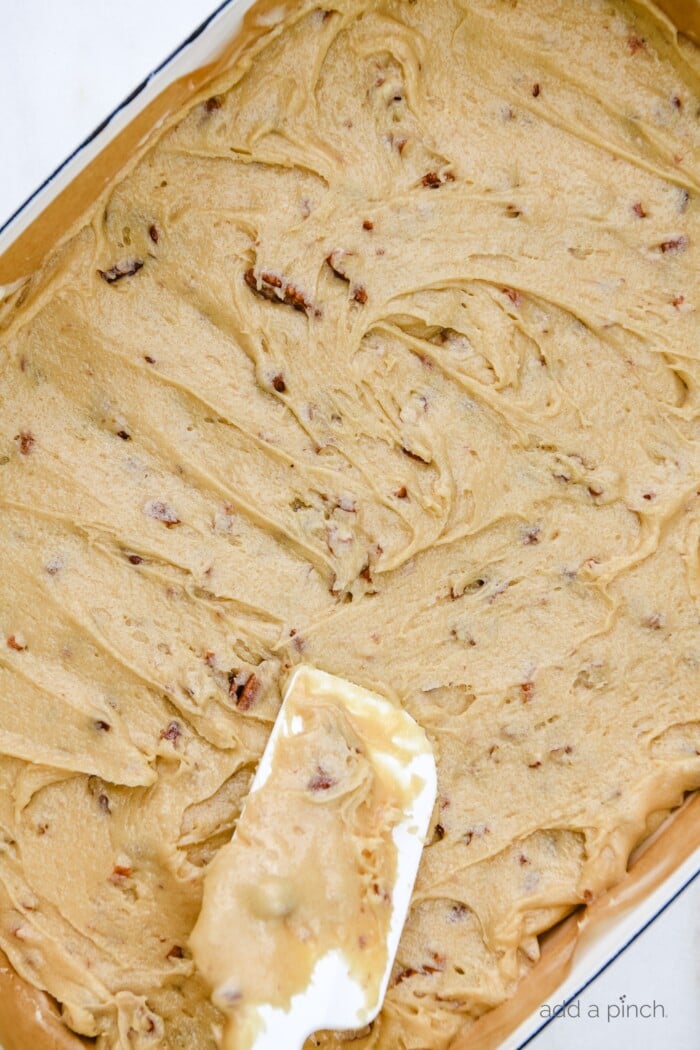 Baking dish full of pecan chewies batter being spread to edges of dish with wooden handled spatula. // addapinch.com