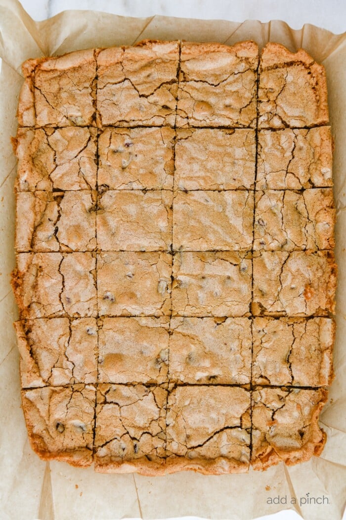 Brown parchment paper lifted from baking pan, with golden baked Pecan Chewies cut into squares  // addapinch.com