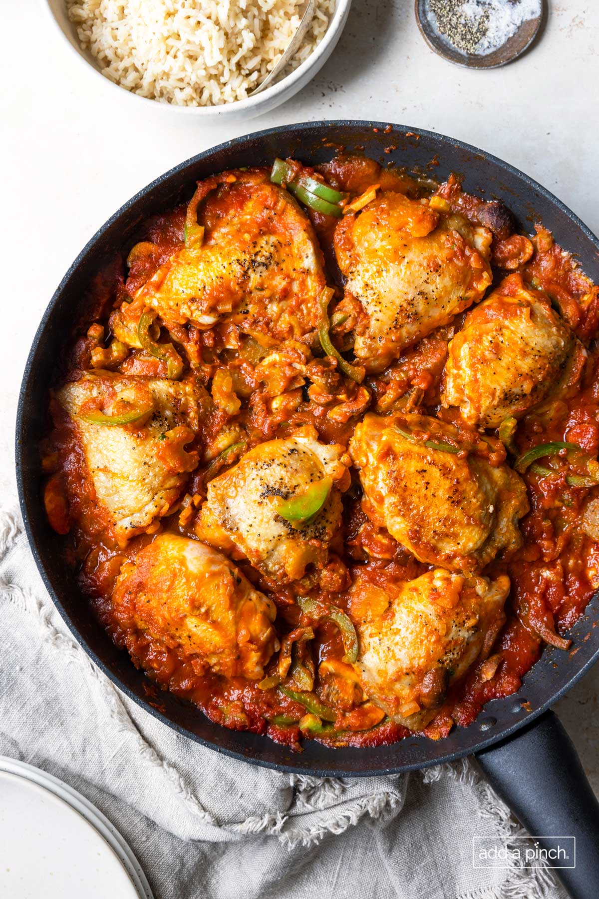 Photograph of chicken cacciatore in a skillet with rice and seasonings in the background ready to serve.
