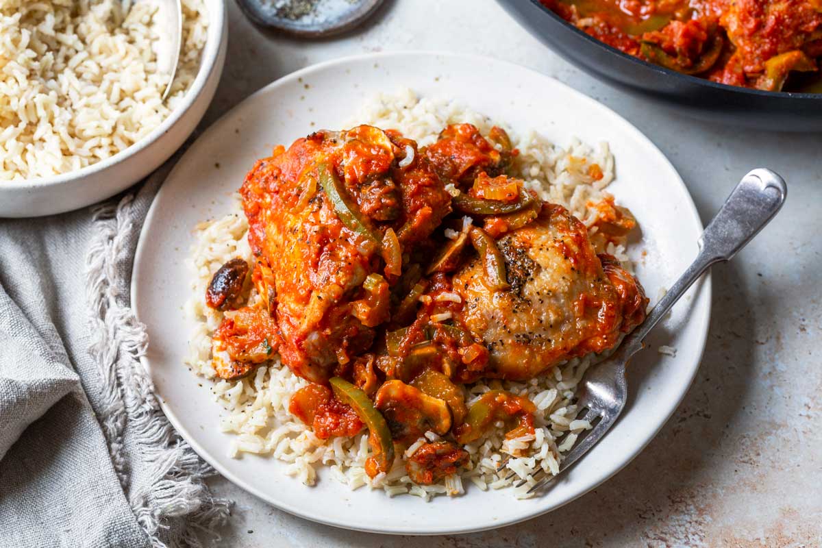 Photo of chicken cacciatore served over rice on a white plate. 