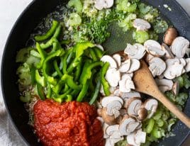 Vegetables, herbs, chicken stock and crushed tomatoes all cooking in a skillet.