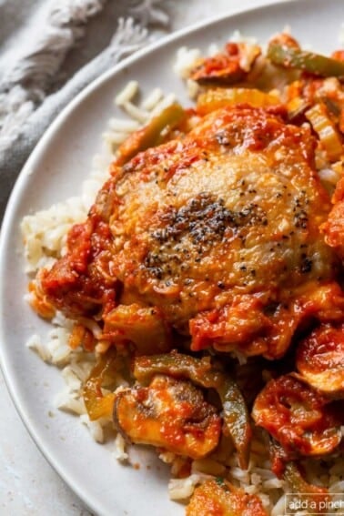 Photo of chicken cacciatore with chicken, peppers, and mushrooms on rice on a white plate.