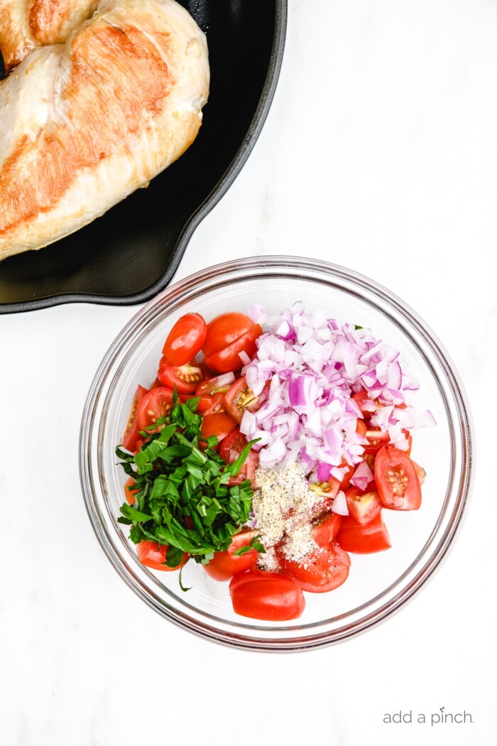 Photo of chicken in a skillet and ingredients to make bruschetta in a bowl.