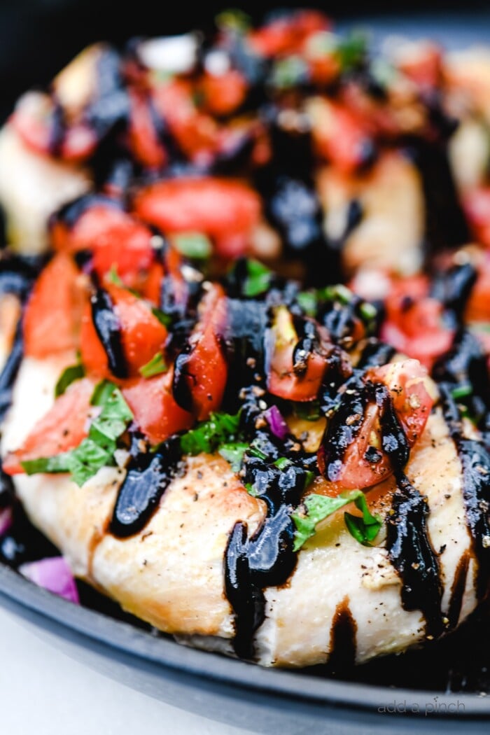 Closeup photograph of chicken topped with bruschetta and balsamic glaze.