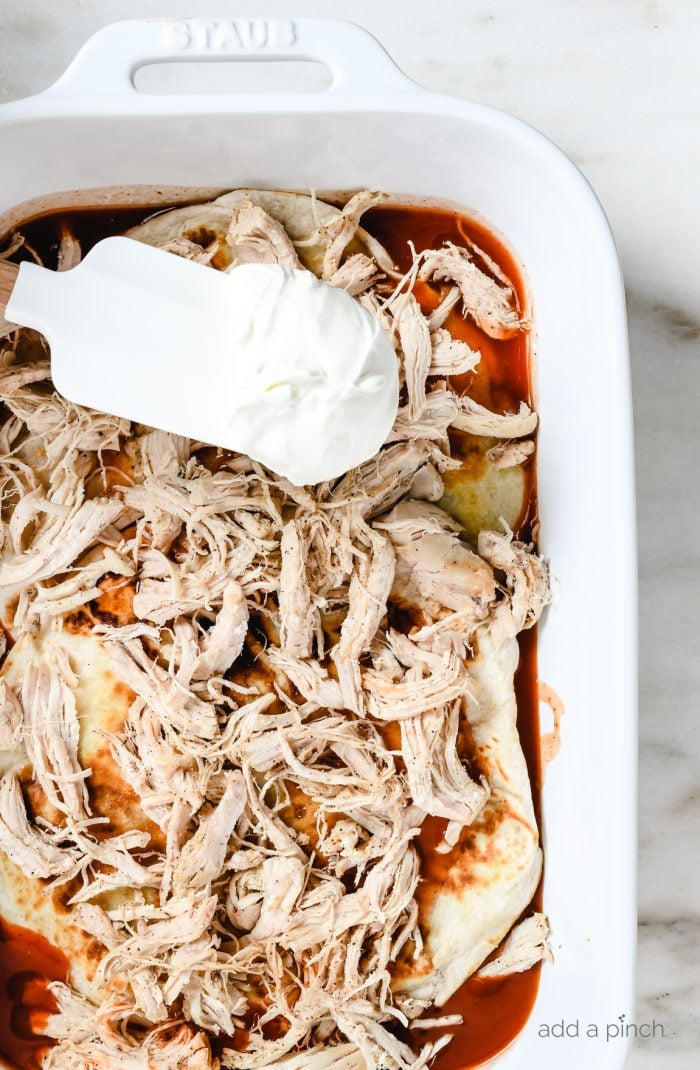 White baking dish layered with enchilada sauce, tortillas, chicken and sour cream // addapinch.com